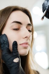 Fototapeta premium Young woman making makeup in a dressing makeup room. Lips make up process. Make-up artist in beauty studio doing makeup for beautiful girl