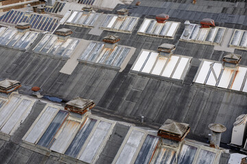 High-angle view of an industrial building's roof, featuring numerous skylights, vents, and a...