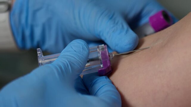 Hands in protective gloves inserting a needle successfully into the skin, accessing the vein, and collecting blood with a vacutainer tube, extreme close up shot.