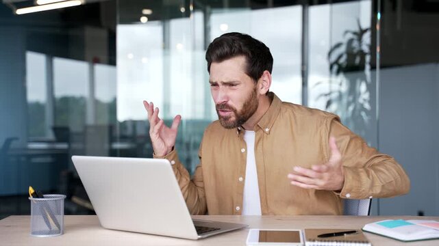 Angry businessman arguing talking on a video call using laptop computer sitting at workplace in business office. Excited dissatisfied executive quarrel shouting with subordinate about problems