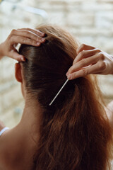 Naklejka premium woman fixing hair with metal hairpin, close-up view, brown hair, soft natural lighting, indoor background, calm atmosphere