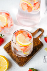 Strawberry lemon infused water in pitcher and glasses served with ice cubes and fresh fruit
