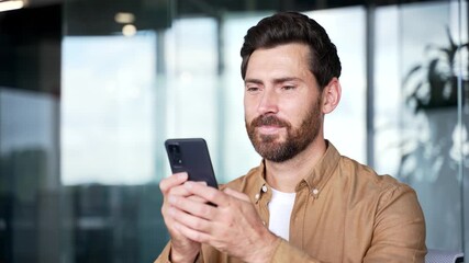 A smiling businessman is using browsing mobile phone at the workplace in a modern business office. Worker is chatting online, working in application or reading writing message on smartphone. Close up - Powered by Adobe