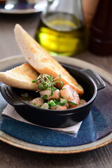 Black bowl with shrimps, fresh herbs, and baguette, served in a restaurant. A close-up view of a delicious seafood dish, beautifully styled and plated for gourmet dining.