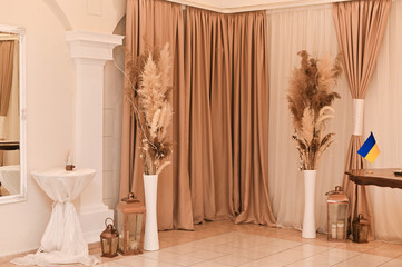 Minimalist room with warm beige curtains, decorative columns, and dried floral arrangements....
