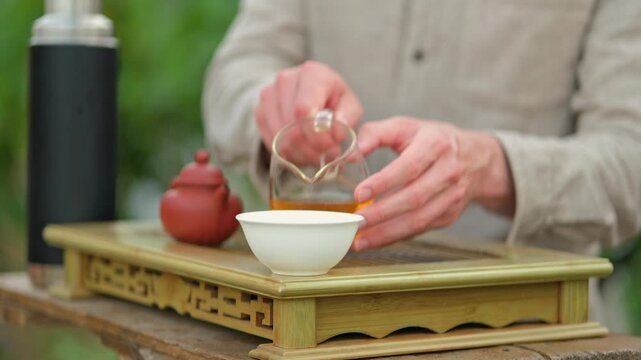 Close up shot of a man standing behind chaban, pouring tea from glass chahai into white tea cup, shallow depth of field