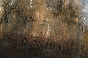 Close-up of water droplets on foggy window, showing texture of wet glass. Condensation on cold glass surface with water drops, creating abstract blurred background with natural pattern.