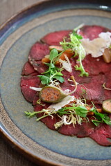 Close-up view of beef carpaccio with parmesan, served on a rustic plate in a restaurant setting, showcasing raw meat delicacy and elegant food presentation.