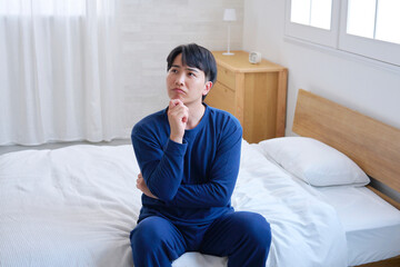 Fototapeta premium ベッドに座る20代男性 考える