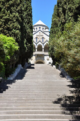 Majestic view of a wide stone staircase leading to the entrance of a historic church framed by tall green cypress trees. Religious architecture.