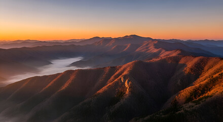 Fototapeta premium A breathtaking panoramic view of a majestic mountain range during a serene golden hour sunrise, with warm light illuminating the peaks and a sea of fog resting in the valley below