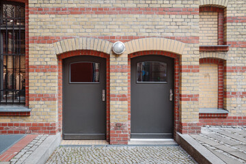 A symmetrical photograph of two identical gray doors set side-by-side in a historic brick building...
