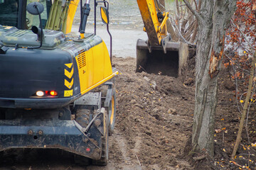Excavator digs soil with bucket at construction site with trees. © Александр Ланевский