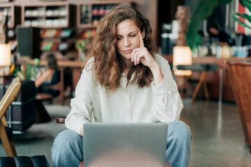 A businesswoman sitting in a coffee shop works online using a laptop.