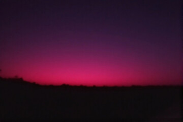 Naklejka premium A breathtaking time lapse of a vibrant orange and red sunset over dark mountain silhouettes as sunlight fades through clouds across the evening sky.