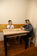 Mother and son sitting at table, drinking tea and enjoying cookies together, spending family bonding time in cozy home interior