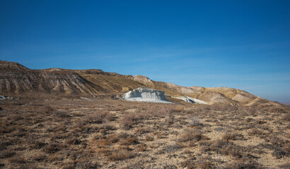 Breathtaking arid landscape featuring layered rock formations, white chalk cliffs, and dry vegetation under a vibrant blue sky.