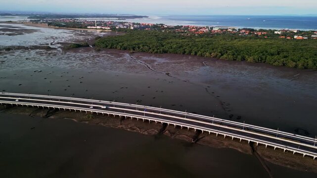 From high above Bali Mandara Toll road extends over vast stretches of mud revealed by low tide the drone video captures the balance of modern highway design with surrounding tropical seascape
