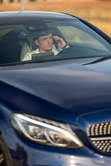 Fototapeta premium Confident young man in white shirt making phone call inside elegant blue luxury car front view