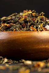 green tea poured into a wooden cup with the addition of fruits and berries, dry high-quality expensive tea in a wooden bowl