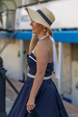 A girl with blond hair dressed in vintage nautical style dresses on the embankment of the river...