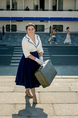 A girl stands with a suitcase in her hands on the embankment of the river station, port.