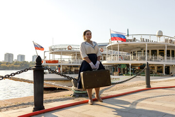 A girl stands with a suitcase in her hands on the embankment of the river station, port.