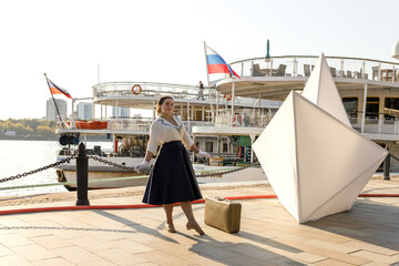 A girl stands with a suitcase in her hands on the embankment of the river station, port.
