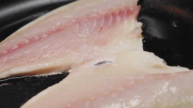 Preparing cod fillets on the stovetop in a cast iron skillet, cover with boiling oil. Cooking at home. High quality 4k footage