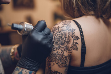 tatto artist tattoing a flower on female shoulder