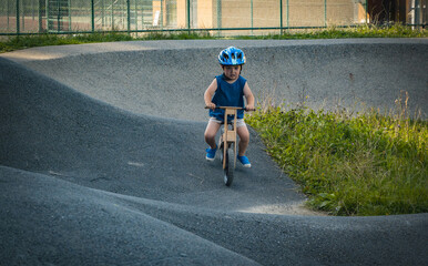 Child wearing a helmet on a balance bike overcomes obstacles on a pump track, having a great time
