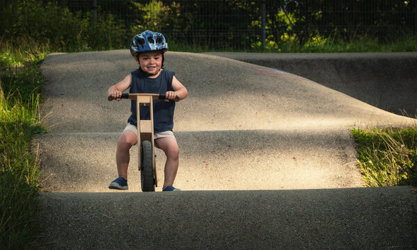 Delighted and joyful boy on a balance bike with a helmet learns to ride a pump track