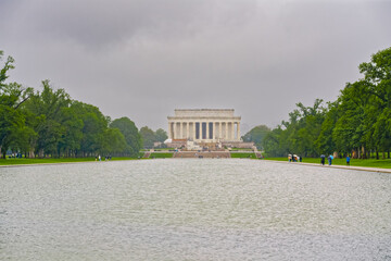 The Lincoln Memorial stands at the far end of the Reflecting Pool with visitors walking nearby...