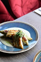 Close-up of a grilled fish fillet served with creamy white sauce and fresh herbs on a plate.