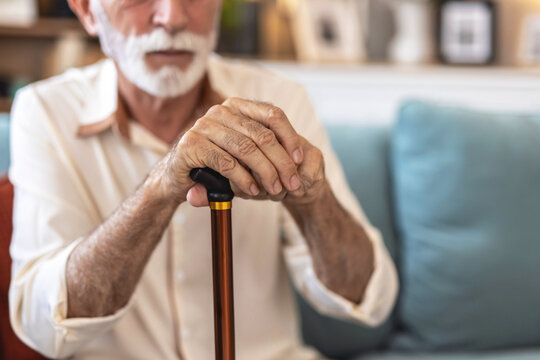 Walking stick, hands and senior man with a disability in home, apartment or retirement with support for injury. Elderly, closeup or person with wood cane to help balance or mobility with arthritis.