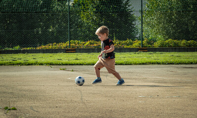Young boy plays with a small ball on the field, the beginning of soccer training