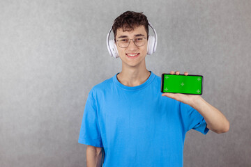 Young man in glasses and headphones holding green screen smartphone in his hands, copy space, chroma key