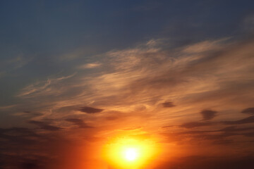 Beautiful colorful dramatic sky with clouds at sunset. Bright orange setting sun low on the horizon. Cirrus clouds change color from blue to yellow to red. Stunning backdrop, gorgeous scenery.