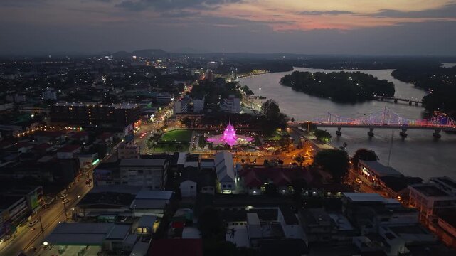 Night aerial of Surat Thani City Pillar Shrine glowing, with city lights, Tapi River, and traffic illuminating the urban landscape of Thailand.