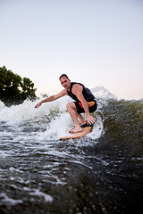 Fototapeta premium Young athletic man energetically riding wakeboard. Handsome caucasian guy glides on the wave like a real surfer. Active lifestyle and extreme sports. Summertime watersports activity.