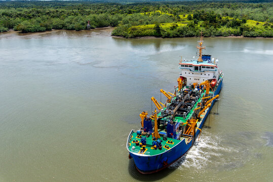 A blue dredging vessel operating on the river near the port of Buenaventura, surrounded by lush tropical vegetation along the riverbanks.