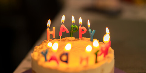Close-up of a birthday cake decorated with colorful candles spelling the word happy, glowing with...