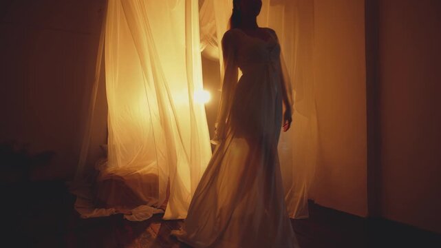Dark shadow silhouette of woman through silk curtains, hands throwing fabric fly in motion, lady walking into night black room. girl behind white curtain. Backlit warm light canopy bed. luxury dress