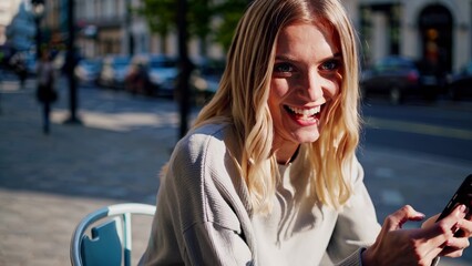 Obraz premium Woman sitting at table with her phone. Woman sitting on the street with smartphone. A casual chatting in the morning with a woman in the morning. A woman at a table using her phone lifestyle.