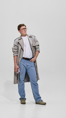 Fototapeta premium Young man in trench coat listening to music with retro cassette player and glasses. Concept of vintage fashion, nostalgia, urban lifestyle and 80s youth culture.
