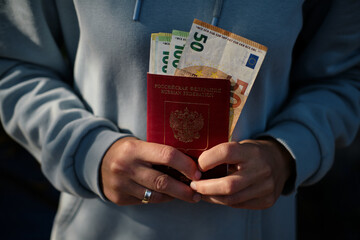 Traveler holding Russian passport with euro banknotes sticking out, close-up of 50 and 100 euro...