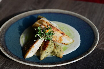 Close-up of a grilled fish fillet served with creamy white sauce and fresh herbs on a plate.