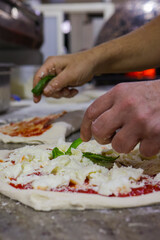 Pizzaiolo napoletano mentre finisce di condire delle pizze tradizionali napoletane su un banco da lavoro in marmo di una pizzeria prima di infornarle