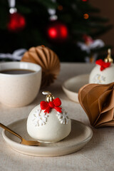 Christmas ball cakes with red bows and snowflakes with cup of tea on a light table with a Christmas tree on a background. Vertical orientation.