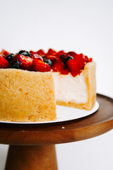Delicious berry cheesecake on a wooden stand with a slice removed for serving